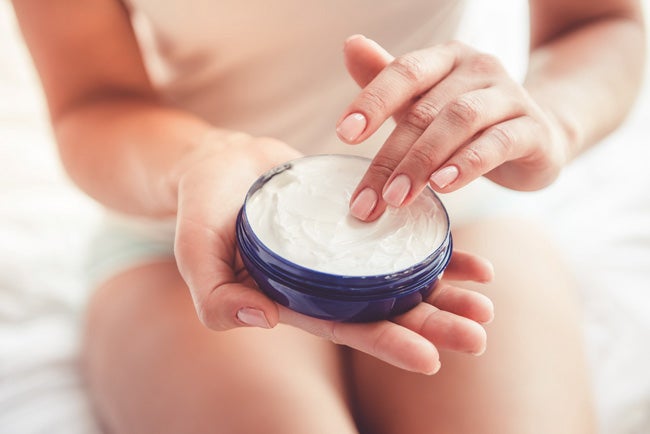 Eine Frau hält eine offene Cremedose in der Hand, um ihr Stoma zu pflegen. 