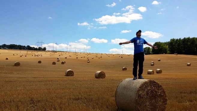 Mann mit Mütze, der auf einem Strohballen steht und seine Arme streckt