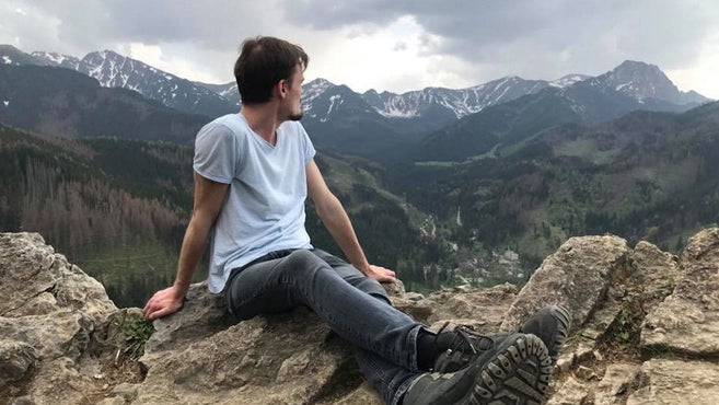 Mann, der auf einem Berg sitzt und ins Tal schaut