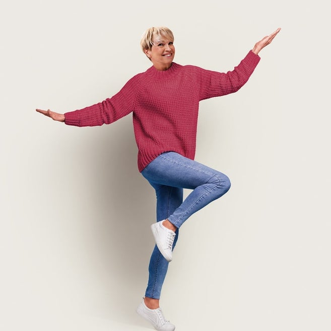 Blonde Frau mit rotem Pullover, die ein Bein beugt und beide Arme ausstreckt