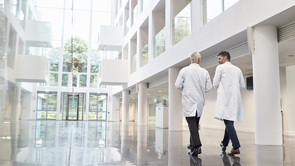 Rear View Of Doctors Talking As They Walk Through Hospital