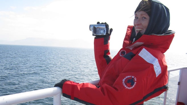 Frau mit dickem Wintermantel und Kapuze, die eine Kamera auf einem Boot hält